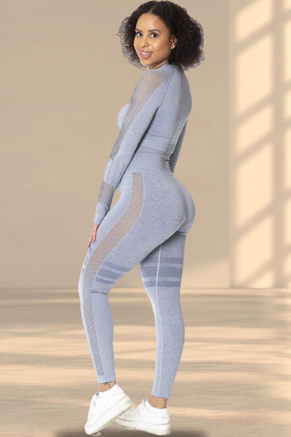 Modellen ser över axeln i grå tights och matchande tröja, med vita sneakers.