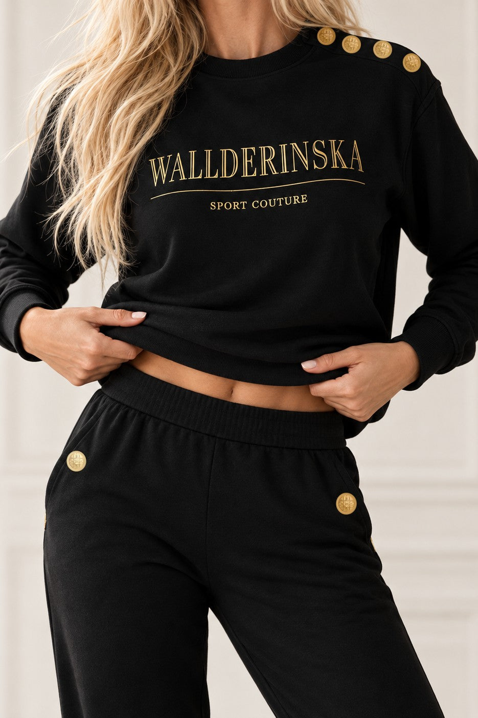 Edge Gold Button Sweater lyft över midjan, med guldknappar på axeln och vid byxornas fickor.