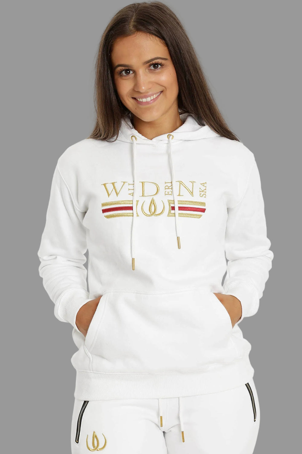 Vit huvtröja med guld och rött broderi över bröstet, buren till vita joggers med guldlogga.