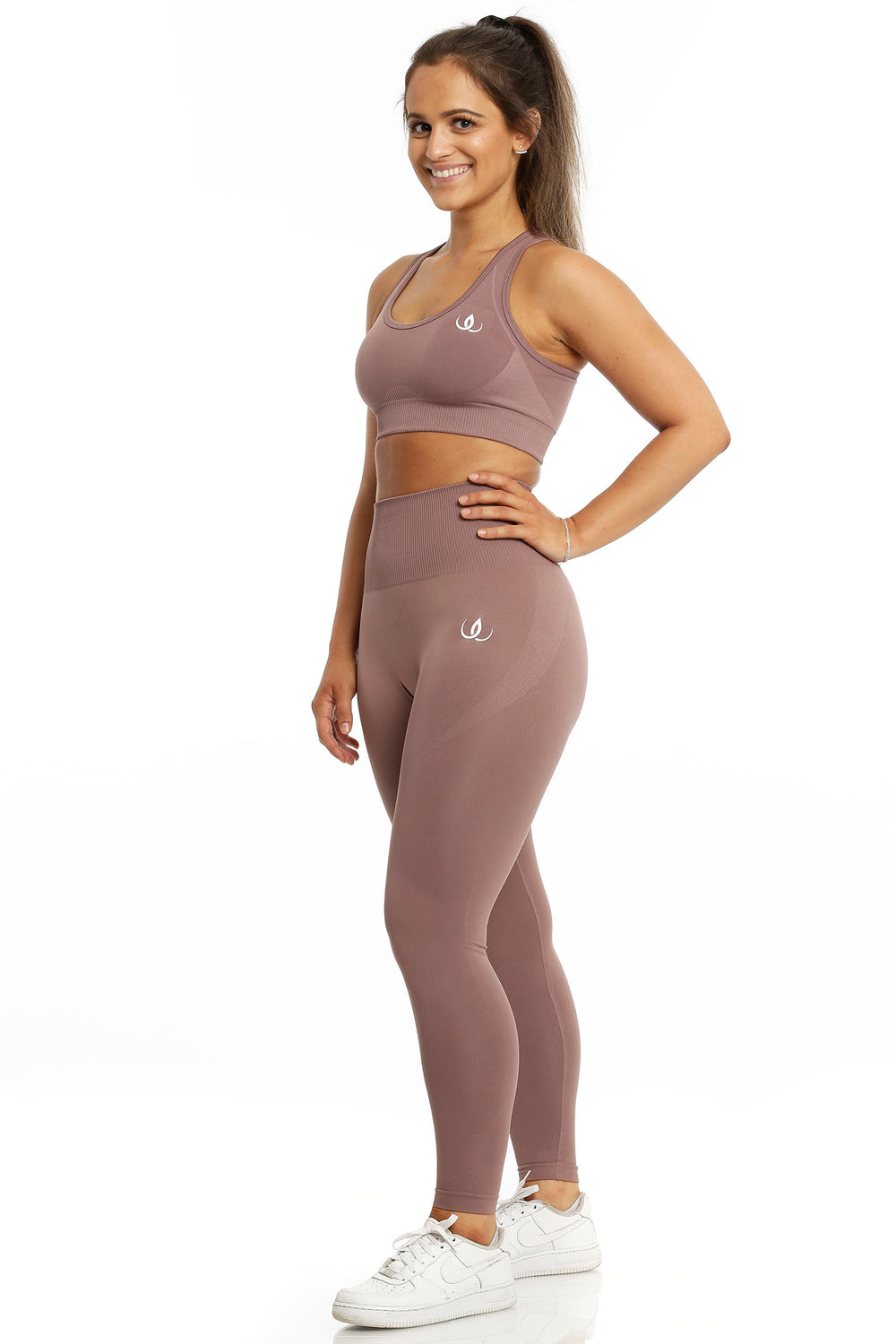 Sport-bh och tights i samma rosbruna ton. Modellen står med handen i sidan, i vita skor.