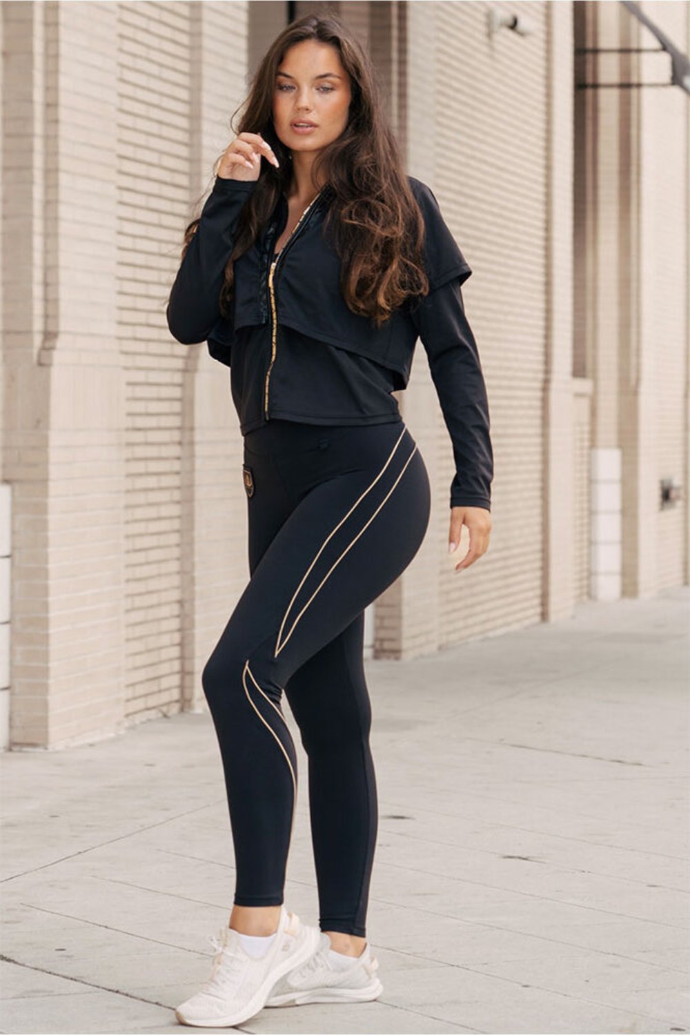 Framför tegelväggen står modellen i jackan och svarta tights med guldlinjer.