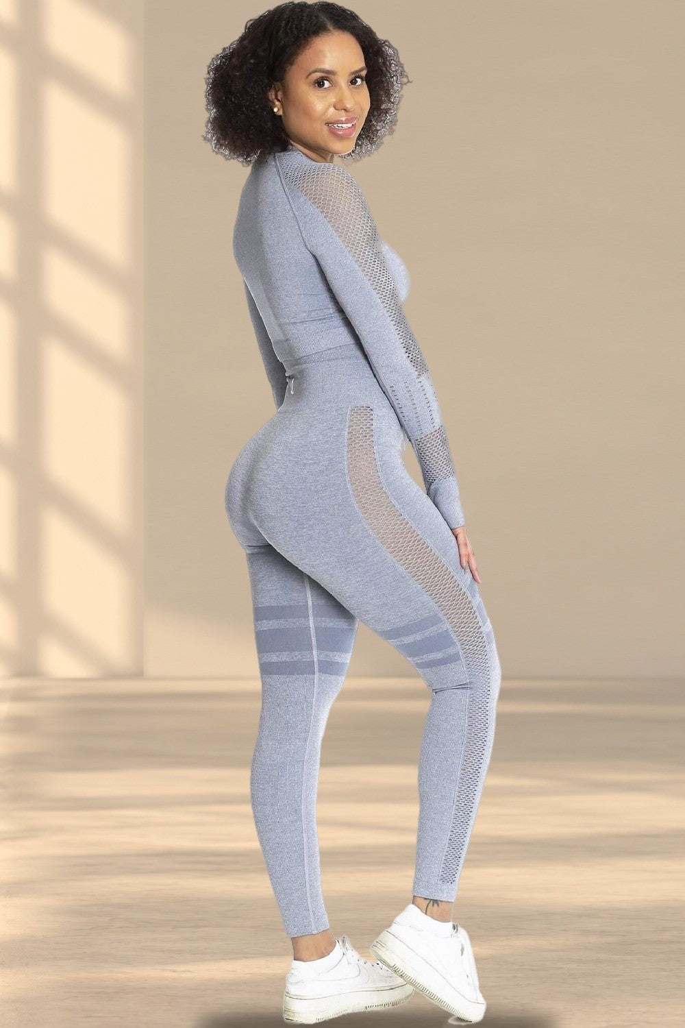 Modellen ser över axeln i grå tights och matchande tröja, med vita sneakers.
